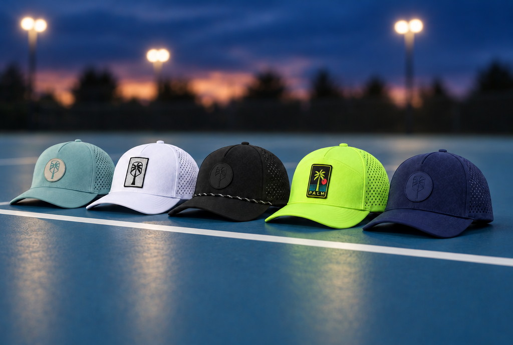 The five new Pickled Palm performance hats lined up on a pickleball court baseline at dusk